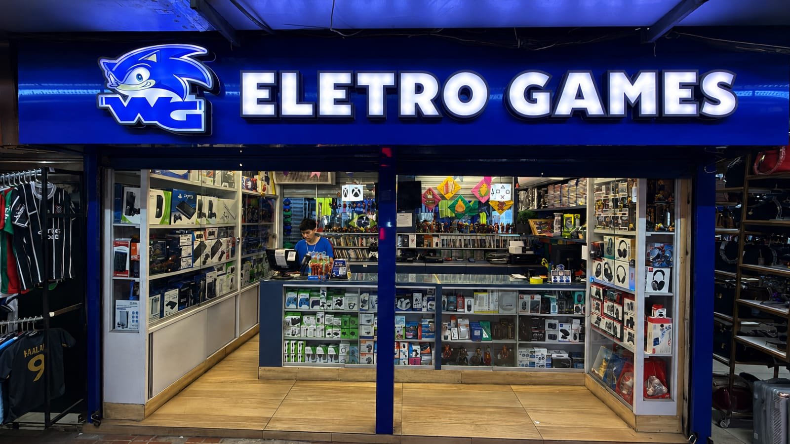 Fachada da loja Eletro Games, com letreiro luminoso e vitrines cheias de consoles, controles e acessórios